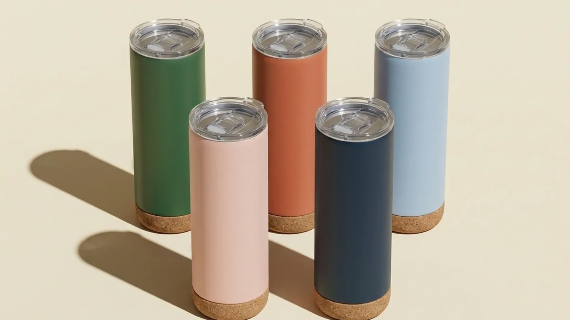 Vasos térmicos de colores con base de corcho sobre fondo crema